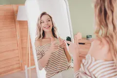 Young blond woman smiling joyfully at her reflection, dressed in a casual striped pullover