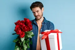 Man holding bouquet of roses and gift standing in front of blue background