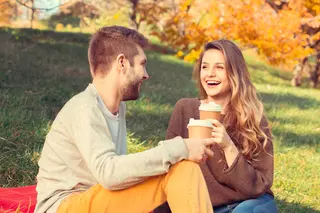 A cheerful couple enjoying a sunny autumn day in the park, sharing laughter and warm cups of coffee