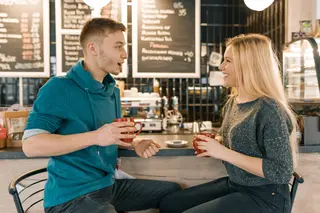 Young smiling man and woman together talking in coffee shop sitting near bar counter