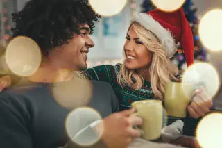 Portrait of young happy couple celebrating Christmas at home with cups of tea on a sofa