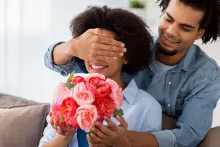 Man presenting flowers to his partner while her covers her eyes