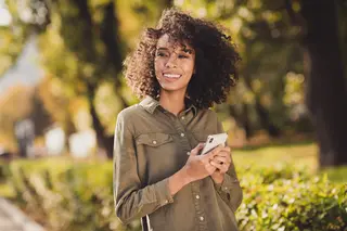 Smiling woman holding a phone wearing a stylish green outfit walking outdoors