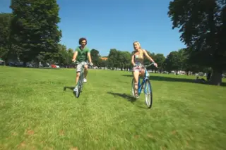 Couple in summer cycling close together in a park with blue sky in background