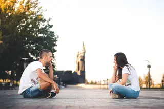 Smiling young couple sitting on park floor opposite each other
