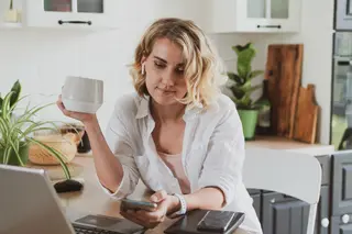 Charming young woman working at home in the kitchen while drinking a cup of coffee