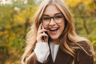 Beautiful young blonde cheerful woman, wearing glasses, wearing a coat talking on mobile phone