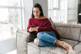 Woman sitting on sofa texting and chatting on her phone