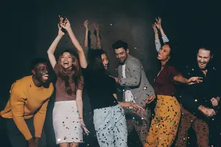 Group of young people dancing and having fun in night club together while confetti flying around