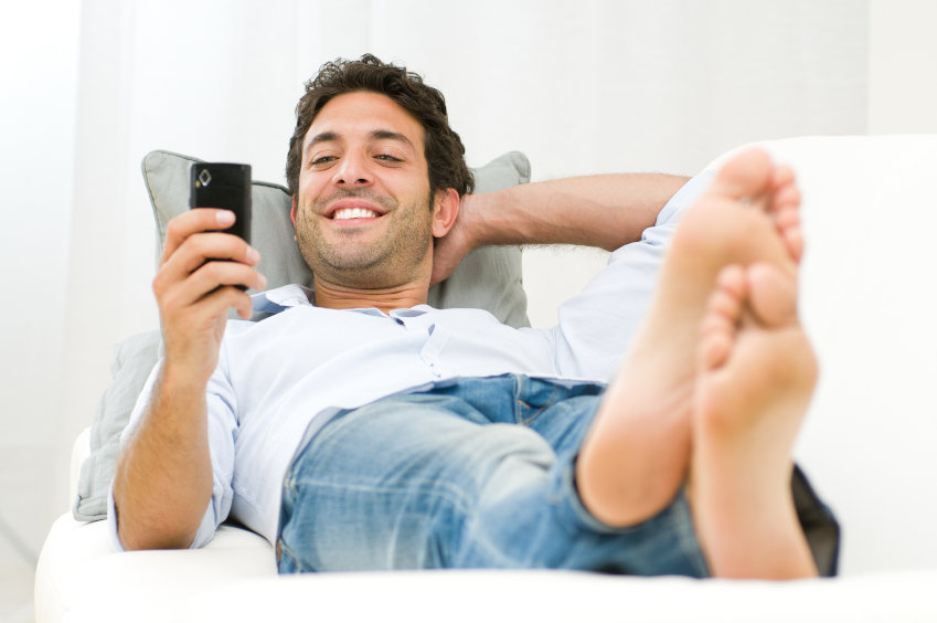 Man lying on sofa smiling whilst texting