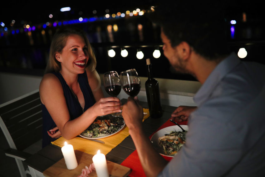 Woman and man at an outdoor table in a restaurant, clinking glasses of red wine