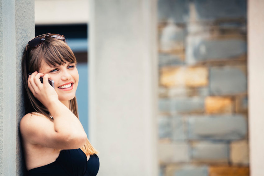 Woman smiling leaning against wall talking on mobile phone