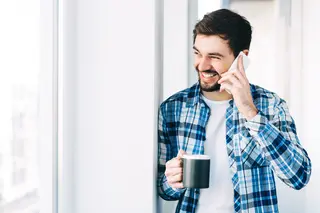 Young man wearing casual clothes talking on a mobile phone in the morning at a window